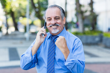 Cheering mexican senior businessman talking at phone