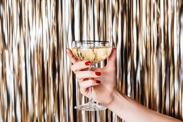 Woman hand is holding champagne glass in the middle of Golden foil tinsel strips. Festive background for christmas, new year, holidays or birthday celebration card.