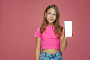 Happy excited little girl child show phone with blank screen mock up on pink background, advertise new mobile apps