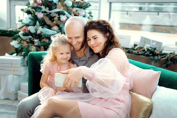 Happy family against Christmas tree enjoing a video phone call with friends and parents. Parents...