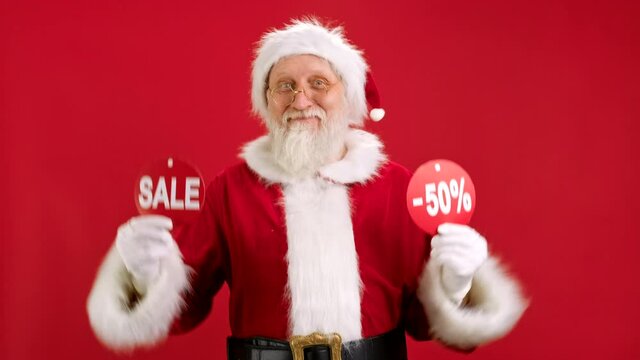 Christmas SALE -50 Off. Cheerful Santa Claus is Dancing and Joyful From Christmas Sale Holding Two Banners With Inscription SALE and -50 Off Showing Off Inscriptions to Camera on Red Background.