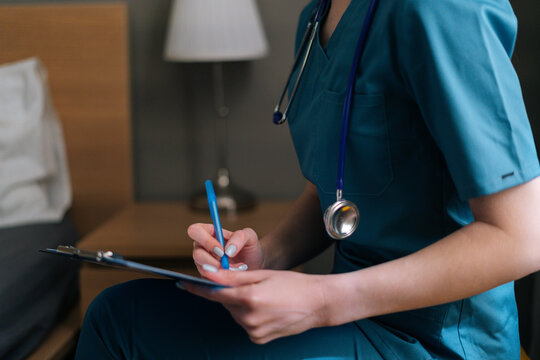 Close-up cropped shot of unrecognizable female doctor writing diagnosis and symptoms in medical history on medical examination in clipboard with pen, selective focus.