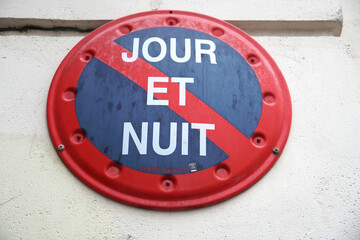 Red and blue street sign indicating a no parking zone day and night (jour et nuit in French).