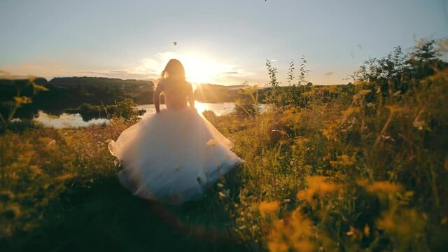 Pretty bride running to the lake on a background of sunset. Moranrange sunset and rays on the backlight. young woman in long chiffon dress