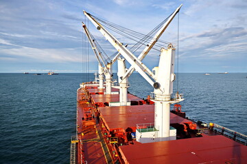 Loading coal from cargo barges onto a bulk carrier using ship cranes and grabs at the port of Muara Pantai, Indonesia. January,2021.
