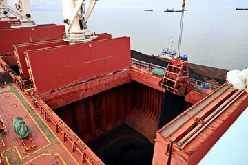 Loading coal from cargo barges onto a bulk carrier using ship cranes and grabs at the port of Muara...