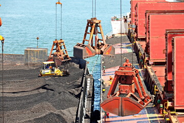 Loading coal from cargo barges onto a bulk carrier using ship cranes and grabs at the port of Muara Pantai, Indonesia. January,2021.