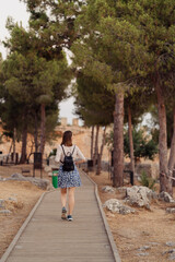 Back view of a woman walking on a wooden path wearing dress and backpack while looking around among trees