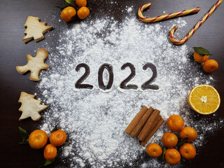 the inscription 2022 on a dark. next to tangerines, orange, cinnamon, caramel, cookies in the form of a Christmas tree and a man. preparing for the celebration of Christmas