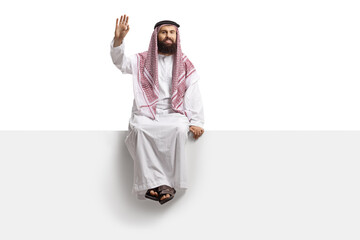 Saudi arab man sitting on a blank panel and waving at camera