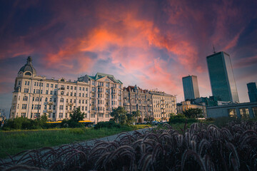 Sunset at Warsaw Centralna station park in late summer, with visible skyscrapers and classical historical buildings in front of train station.
