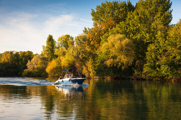 Motorboat with unrecognizable people moving along scenic river in sunny autumn day. Marne river,...