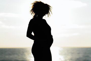 Silhouette of a pregnant woman standing next to the ocean