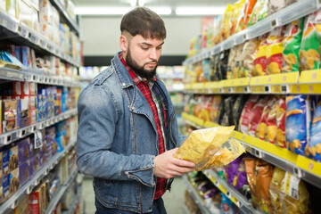 Young bearded man making purchases in grocery store, choosing snacks for beer