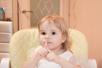 Baby girl celebrates birthday, on a child's chair, shows 2 years with her fingers
