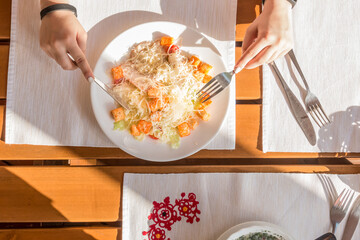 Female hands, caesar salad with ham in a street cafe in the sunbeams top view