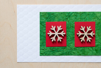 two wooden snowflake ornaments on white, green, and red paper