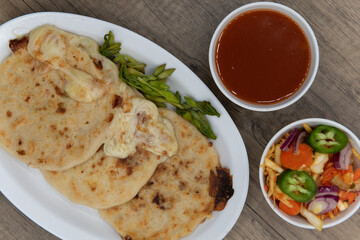 Overhead view of three round pupusas served with salsa and dipping sauce as a Latino food delicacy