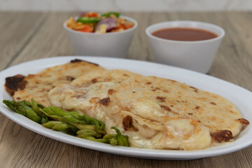 Three round pupusas served with salsa and dipping sauce as a Latino food delicacy