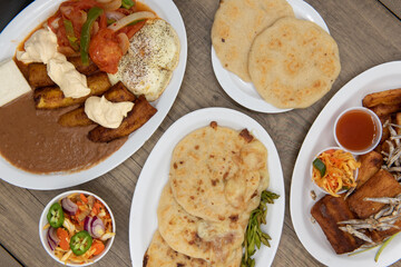 Overhead view of Latino flavored table of prepared El Salvadoran food with meat, fried plantains, pupusa, yucca, and refried beans