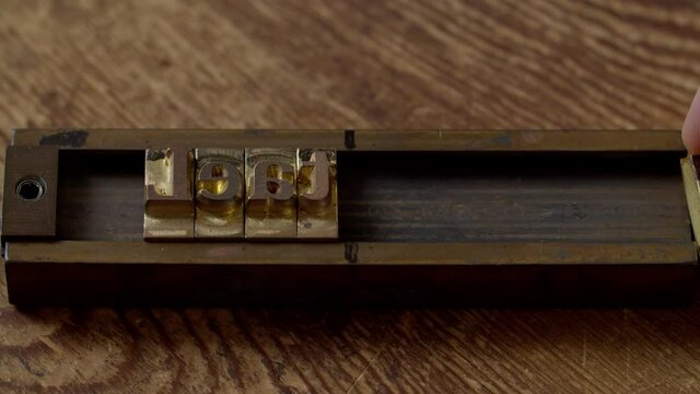 Close-up of worker hands inserting metal symbols into block holder, forming word for heat embossing on leather piece indoors. Workshop employee making cliche for engraving of leather product