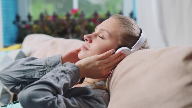Young beautiful woman listening to music in headphones and relaxing on couch. Realtime