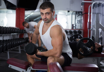 Muscular young man doing exercises with dumbbells at gym