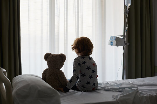 Child patient sitting on bed in hospital room
