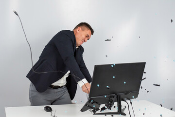 Caucasian man in a suit gets angry and smashes the keyboard on the monitor. An office worker in a rage breaks the computer.