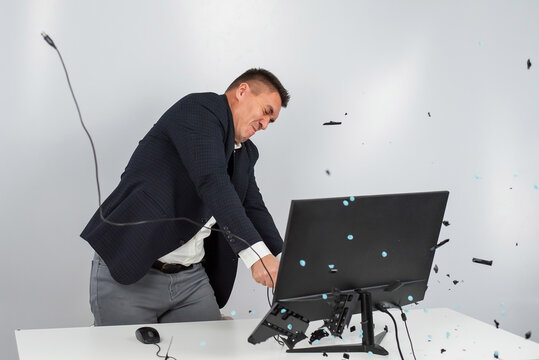 Caucasian man in a suit gets angry and smashes the keyboard on the monitor. An office worker in a rage breaks the computer.