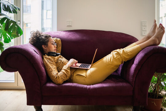 Woman works recklaining on purple sofa