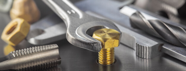 Wrench tightens brass bolt in steel billet. Spanner, bolt, screw and nuts. - obrazy, fototapety, plakaty
