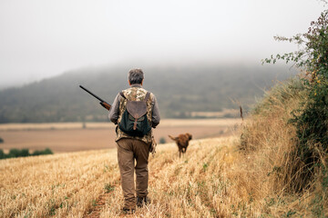 Hunter man and his dog walking on field