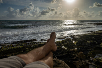 Legs of a young man crossed in a resting pose on a beach during sunrise. - Powered by Adobe