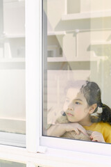 Fototapeta na wymiar Little Asian girl stays home bored by school closings due to covid pandemic. Preschool girl looking outside her home window.