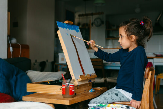 Kid painting on canvas on easel at home living room