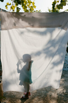 Silhouette of kid behind hanging sheet in sunlight