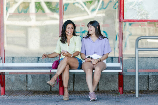 Mother and teen daughter sitting at bus stop