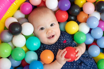 Fototapeta na wymiar Happy child in a ball pit. Baby girl with a ball. 
