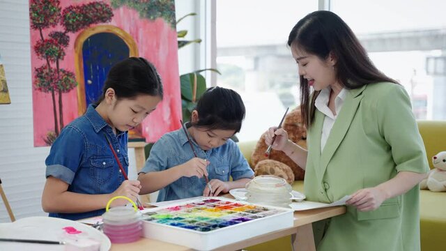 In an art school, a beautiful Asian teacher is teaching children in a painting class, the concept of education.
