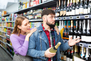 Young family couple deciding what sparkling wine to buy in grocery store. High quality photo