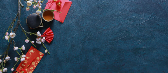 Traditional Chinese tea with red envelopes and blooming plum branches on dark background with space...