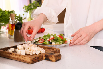 Obraz na płótnie Canvas Woman making Greek salad with cut feta cheese on table in kitchen