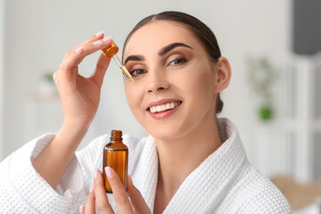 Beautiful woman applying essential oil on face in bathroom