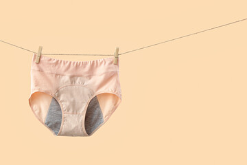 Period panties hanging on clothesline against color background