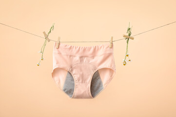 Period panties and chamomile flowers hanging on rope against color background