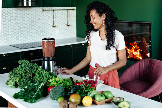 Smiling black woman grinding fruit in blender 