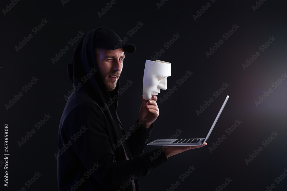 Poster hacker with laptop and mask on dark background