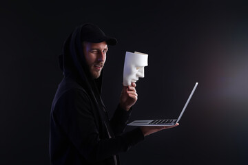Hacker with laptop and mask on dark background
