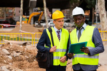 Two workers working at the laying paving slabs facility are carefully studying a folder with important working papers while ..holding it